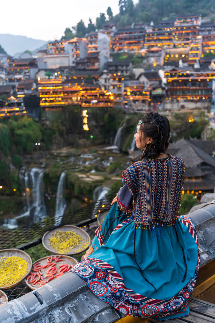 Mujer de espaldas con vestimenta tradicional asiática , observando un paisaje montañoso con edificaciones